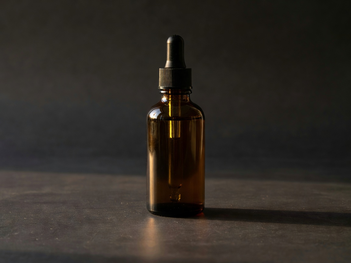 Amber glass dropper bottle on a dark surface lit by warm side light